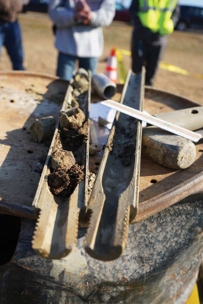 Open split spoon sampler with soil samples and other geotechnical engineering tools.