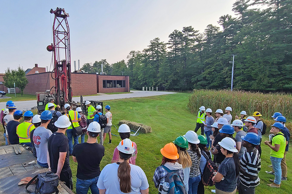 A group of college students look toward drill rig during a geotechnical drilling demonstration on campus.