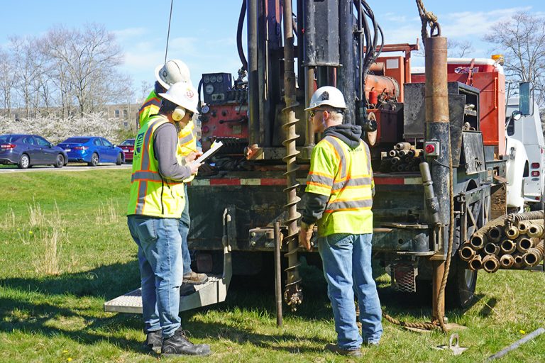 A geotechnical engineer confers with a driller while the drilling assistant looks on.