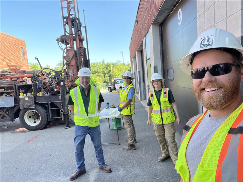 Four employees wearing safety gear at the site of a geotechnical engineering project.