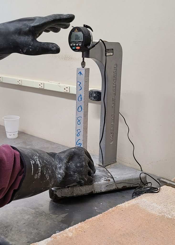 Technician using a length comparator to measure the length of prepared samples before and during the ASR test.