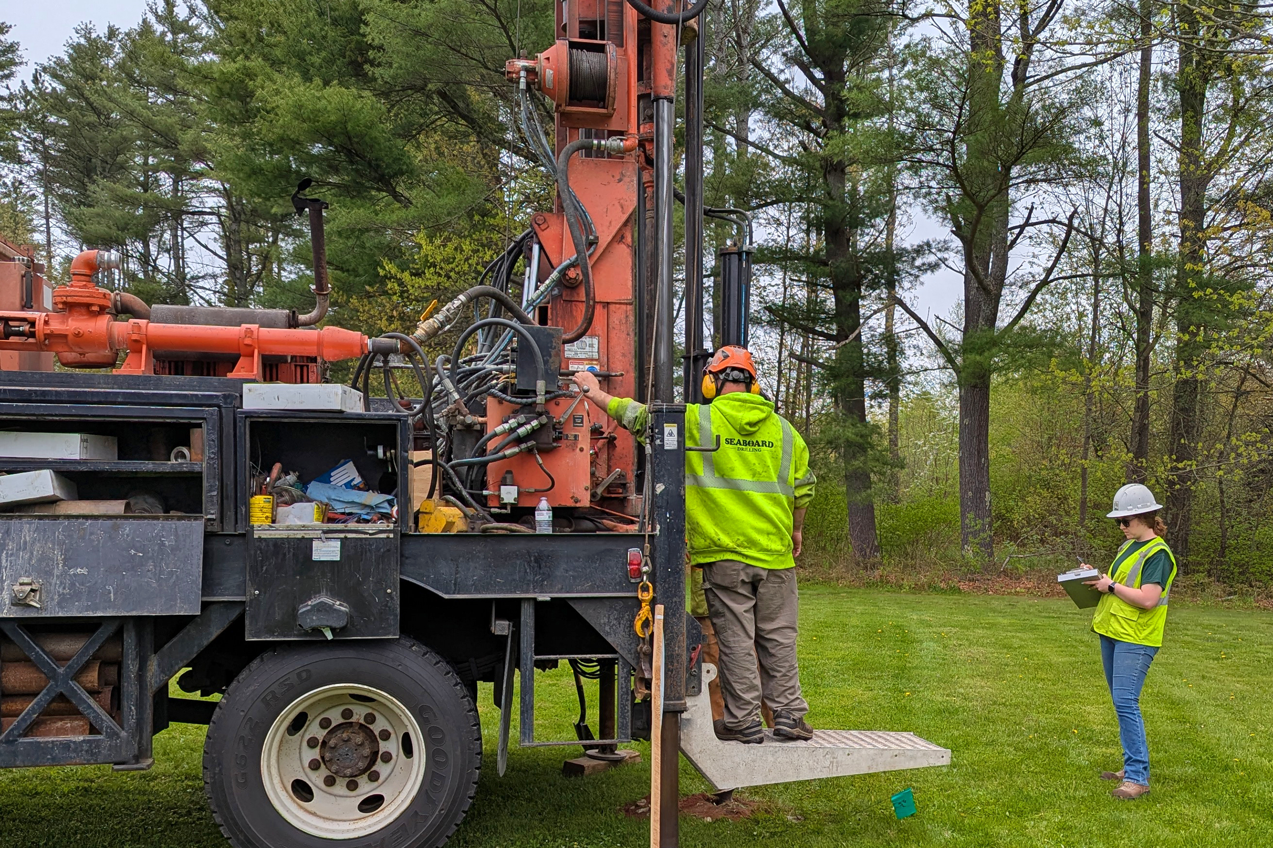 A geotechnical engineer writing on a clipboard while observing a geotechnical drilling rig.