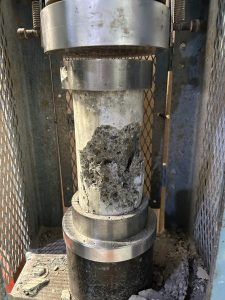 A broken concrete cylinder in a compression machine.