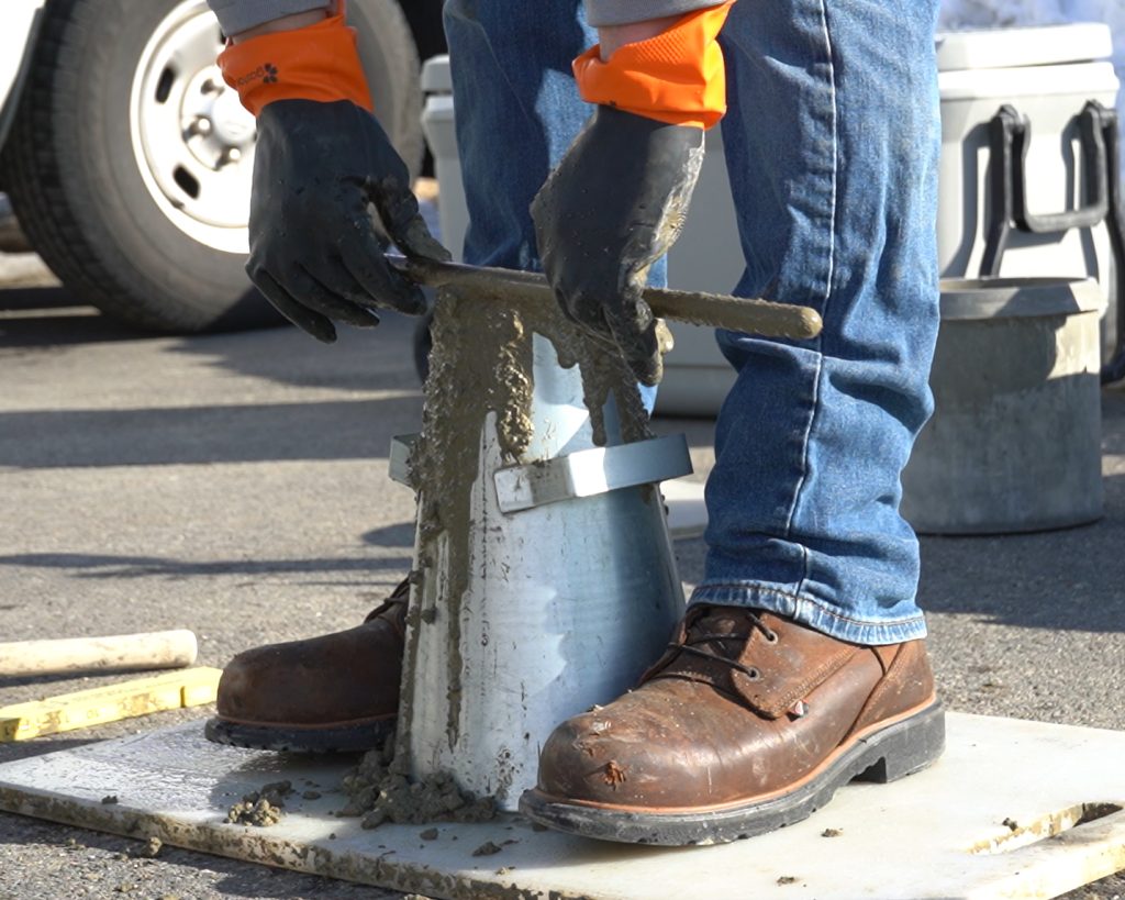 Close up view of a construction materials technician completing a slump test on fresh concrete.
