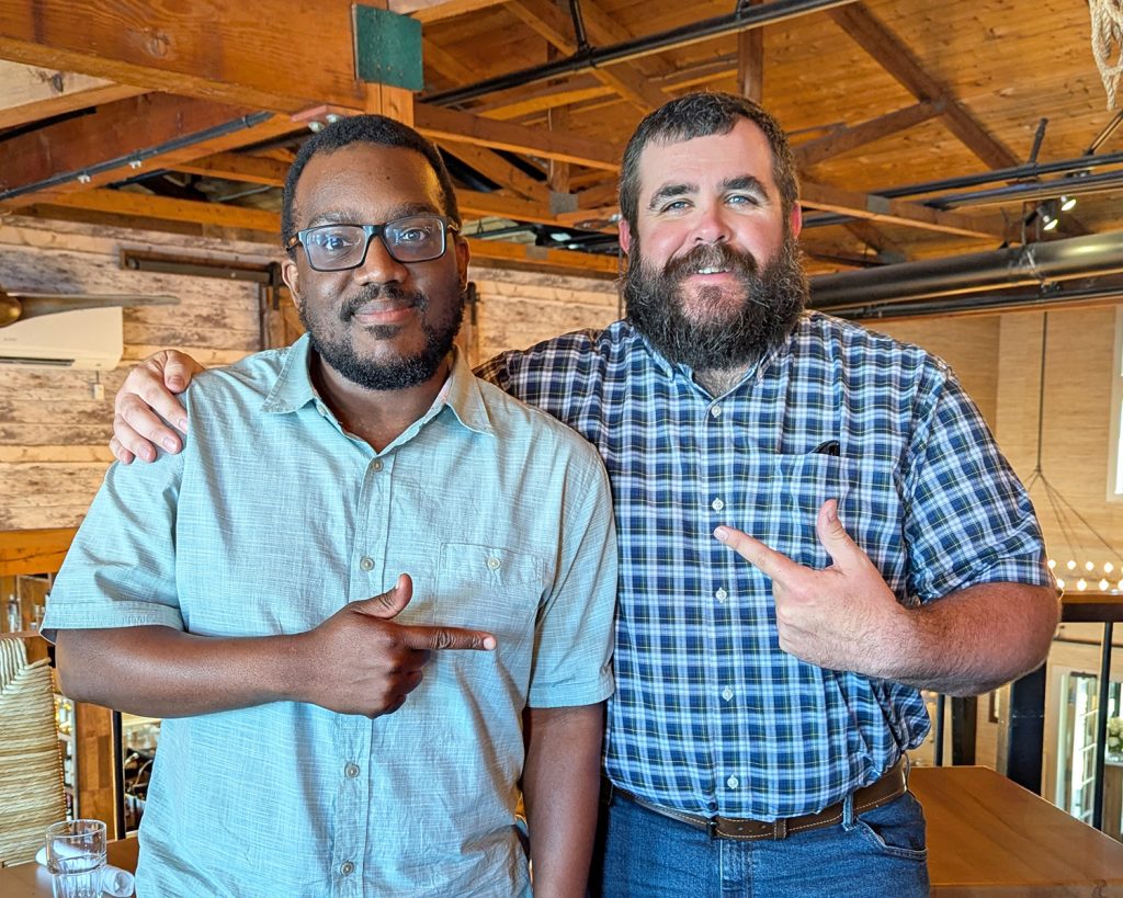 Jethro Celamy with his Emerging Leaders mentor, Evan Walker, pointing at each other and smiling in an indoor space.