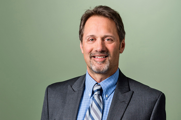 Paul Kohler in formal business attire with a light green background.