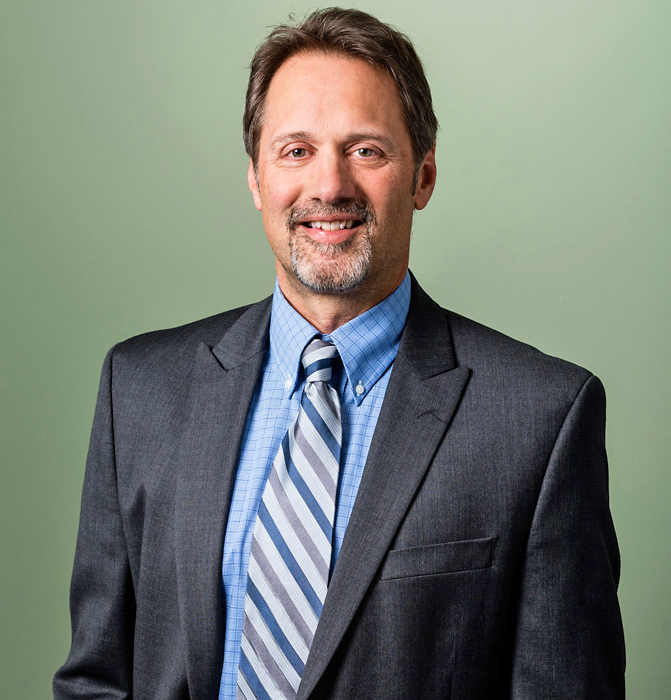 Paul Kohler in formal business attire with a light green background.