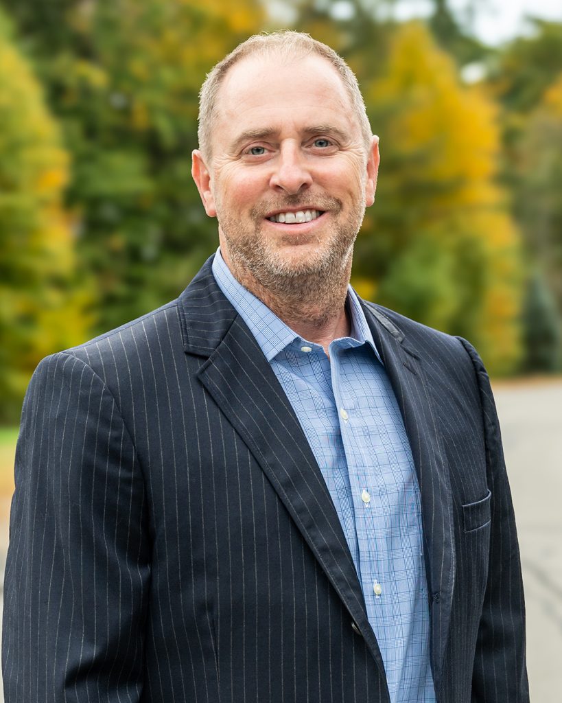 Photo of Chad Michaud with fall leaves and a road in the background.